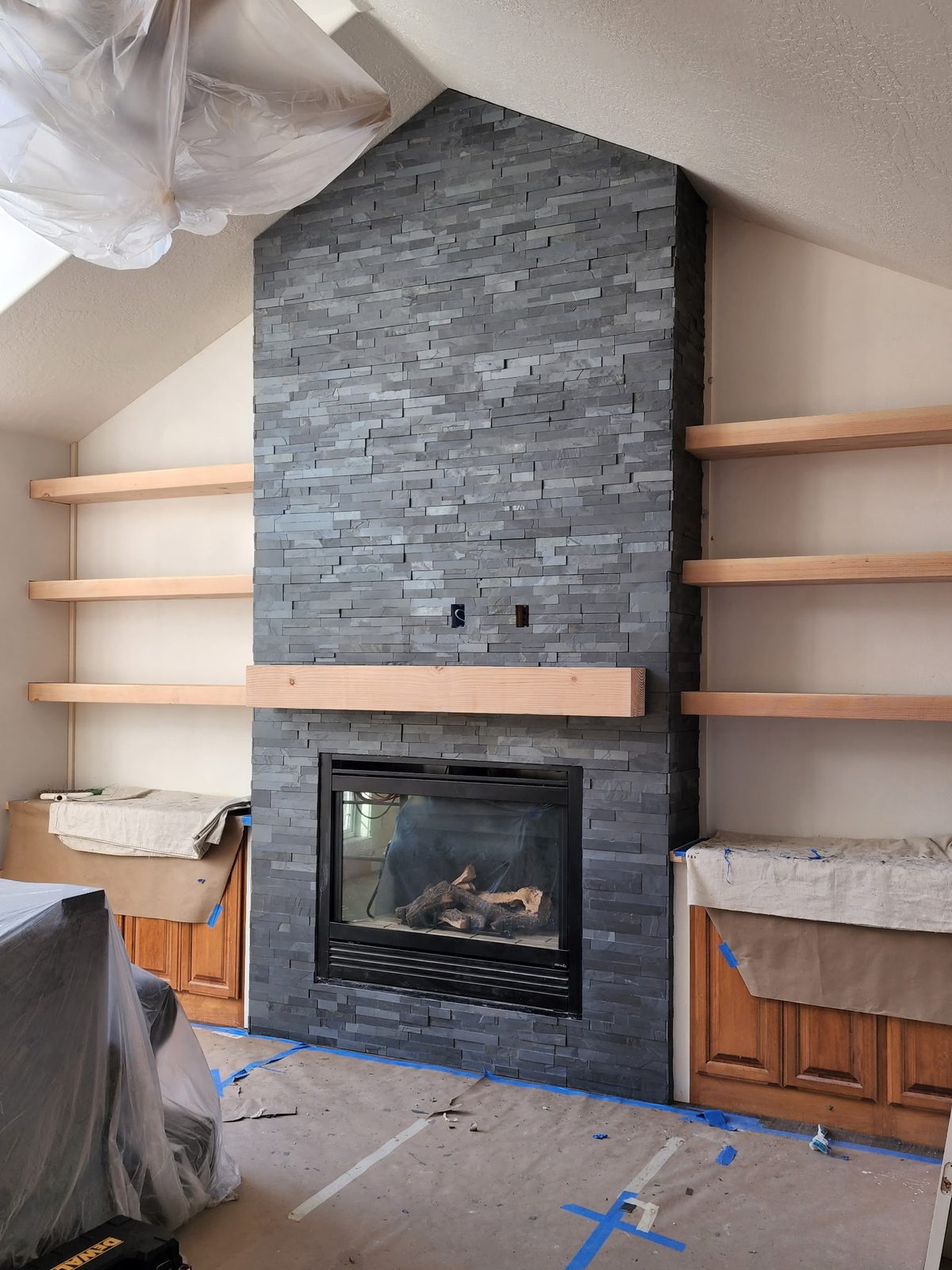 Charcoal stacked-stone floor-to-ceiling fireplace with wood mantel and floating shelves
