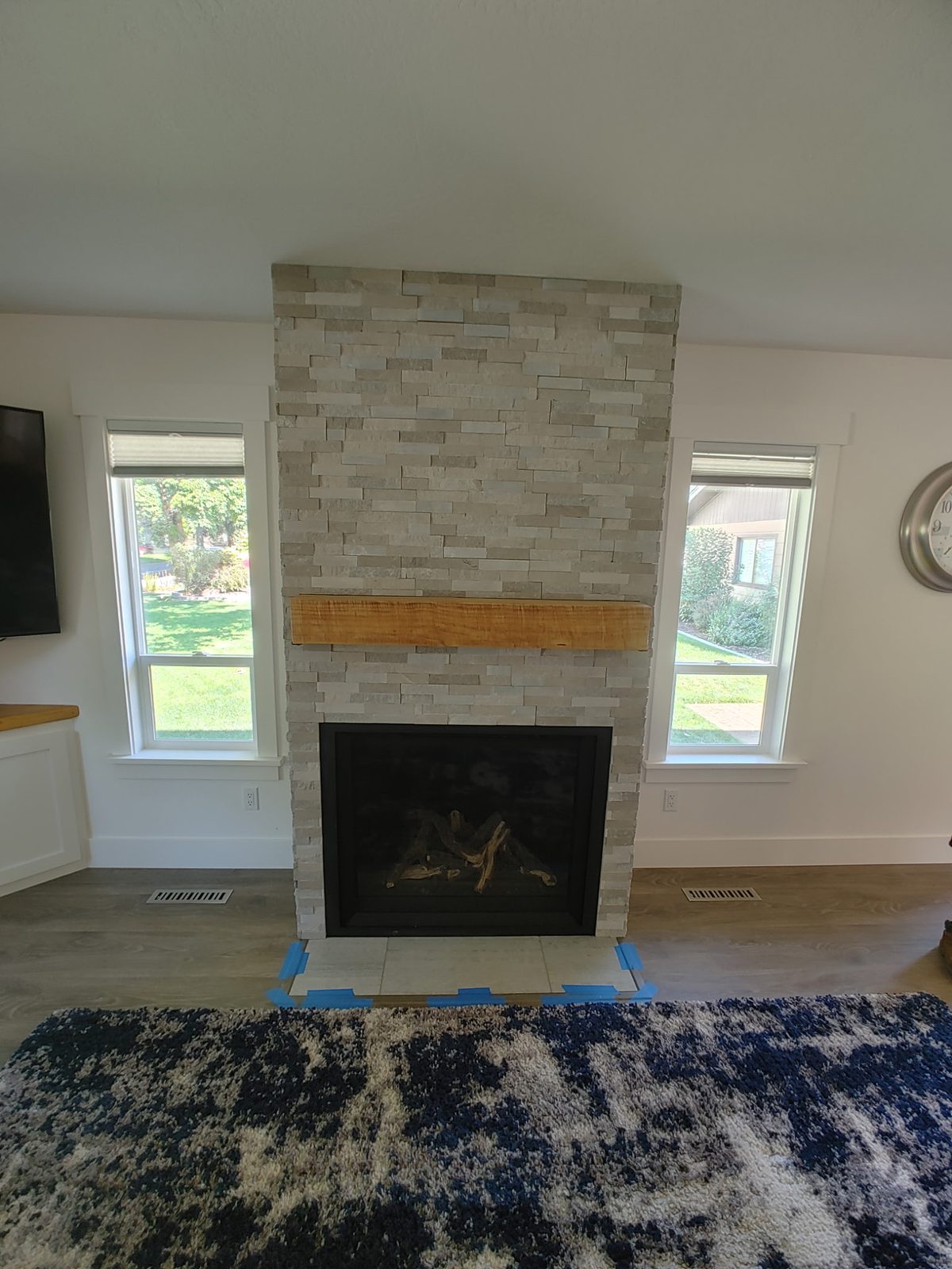 Light stacked-stone fireplace with live-edge wood mantel between two windows
