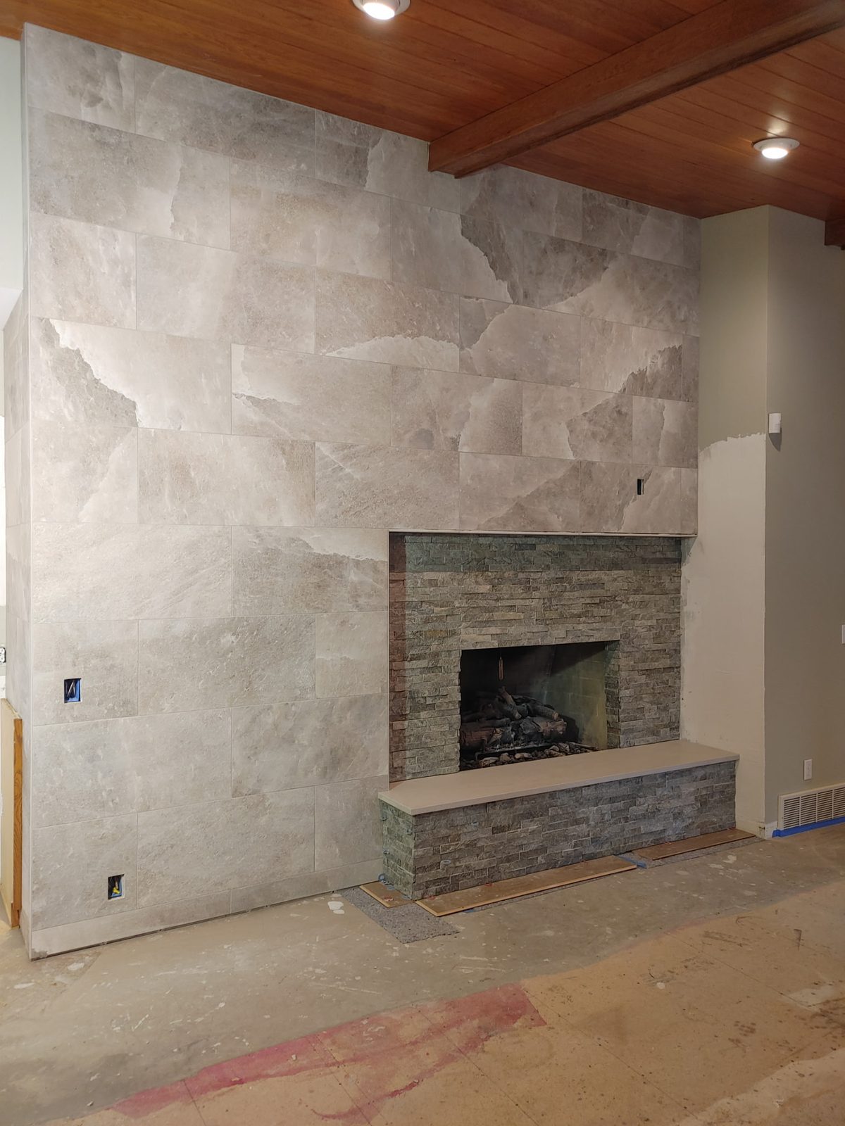 Large-format marble-look porcelain fireplace wall with stacked-stone firebox and hearth bench
