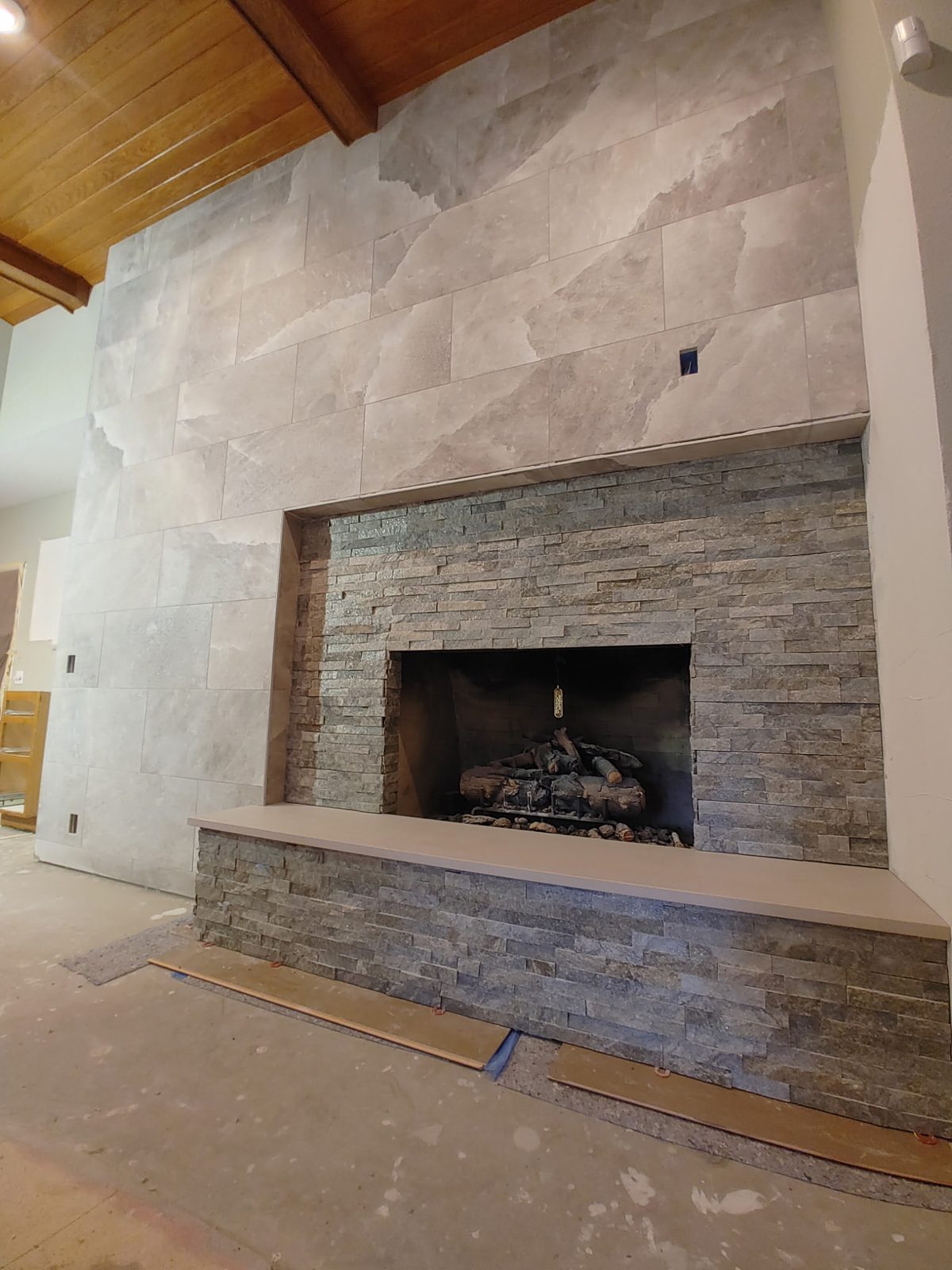 Floor-to-ceiling gray porcelain fireplace with stacked-stone firebox and long hearth bench