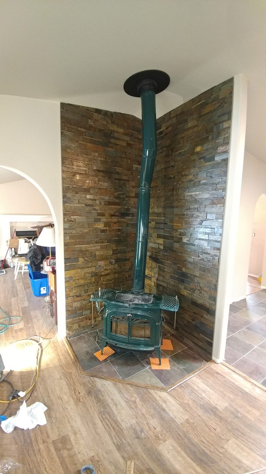 Green enamel wood stove with slate stacked-stone corner surround and hearth