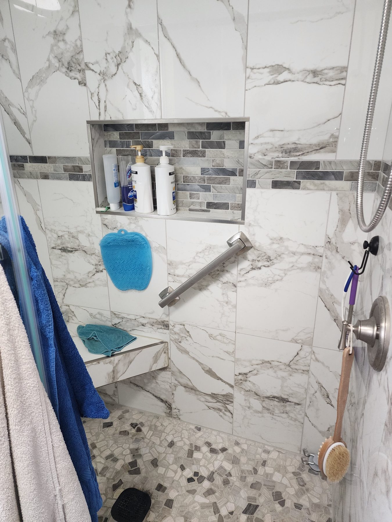 Marble-look tile shower with glass mosaic accent band and recessed niche