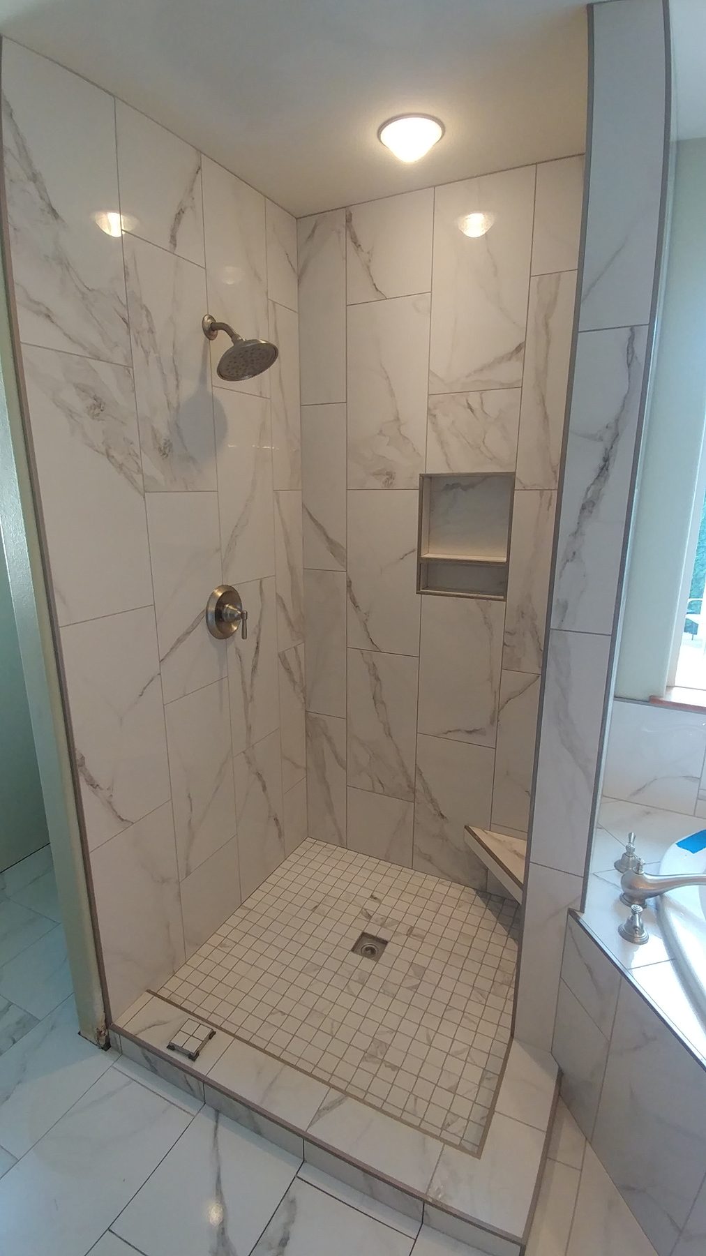 Marble-look tile walk-in shower with recessed niche